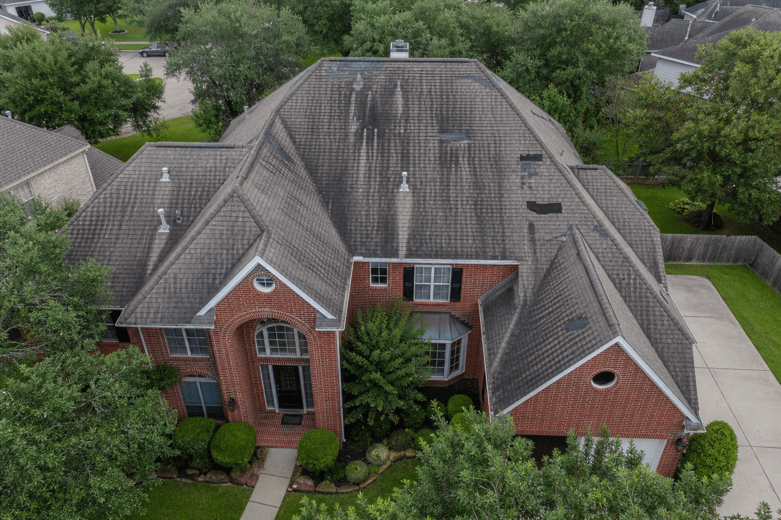 Illustrative example of an aged, weather-damaged residential asphalt shingle roof in suburban Houston with visible algae streaks and missing shingles